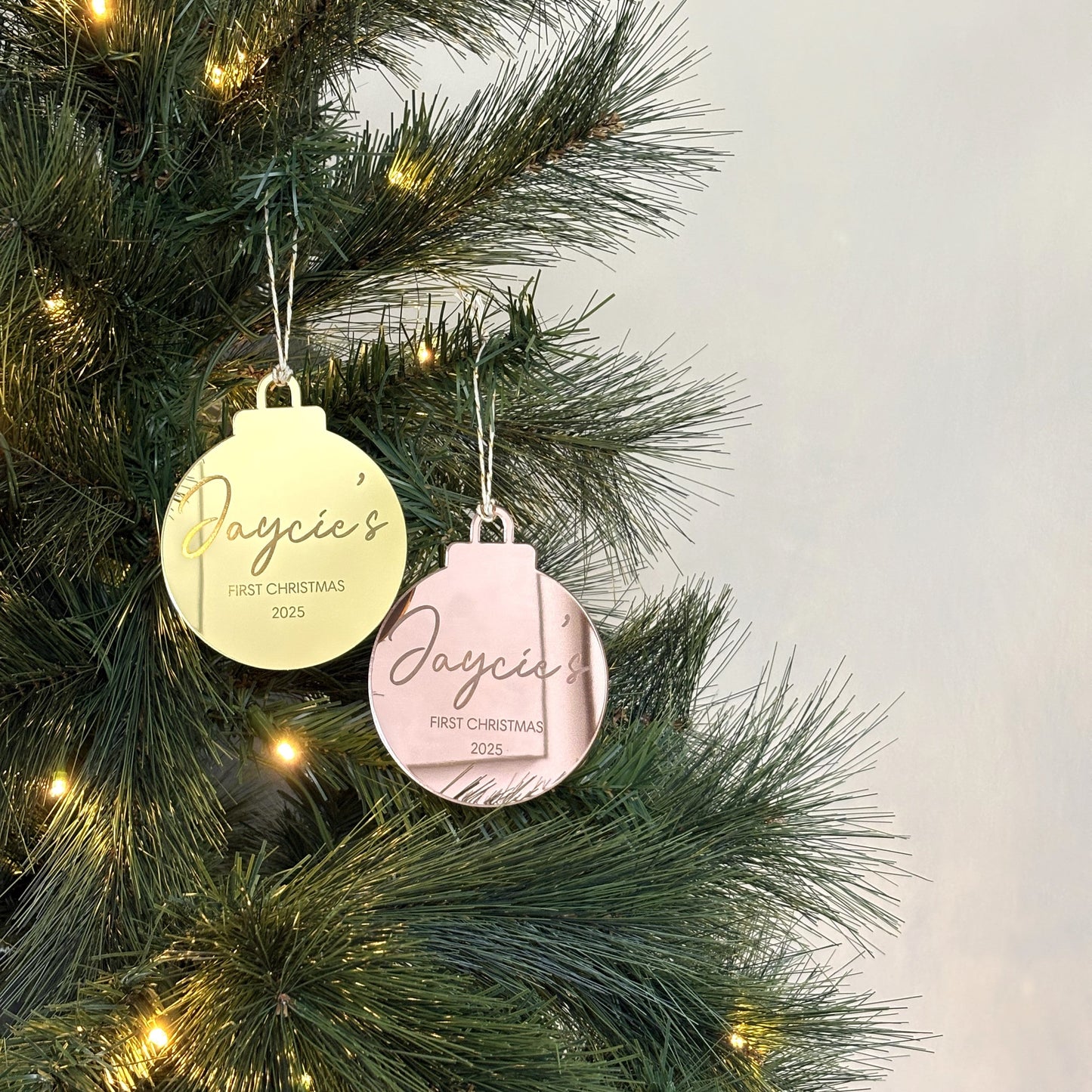 Two Christmas ornaments on a decorated tree with a light gray background