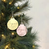 Two Christmas ornaments on a decorated tree with a light gray background